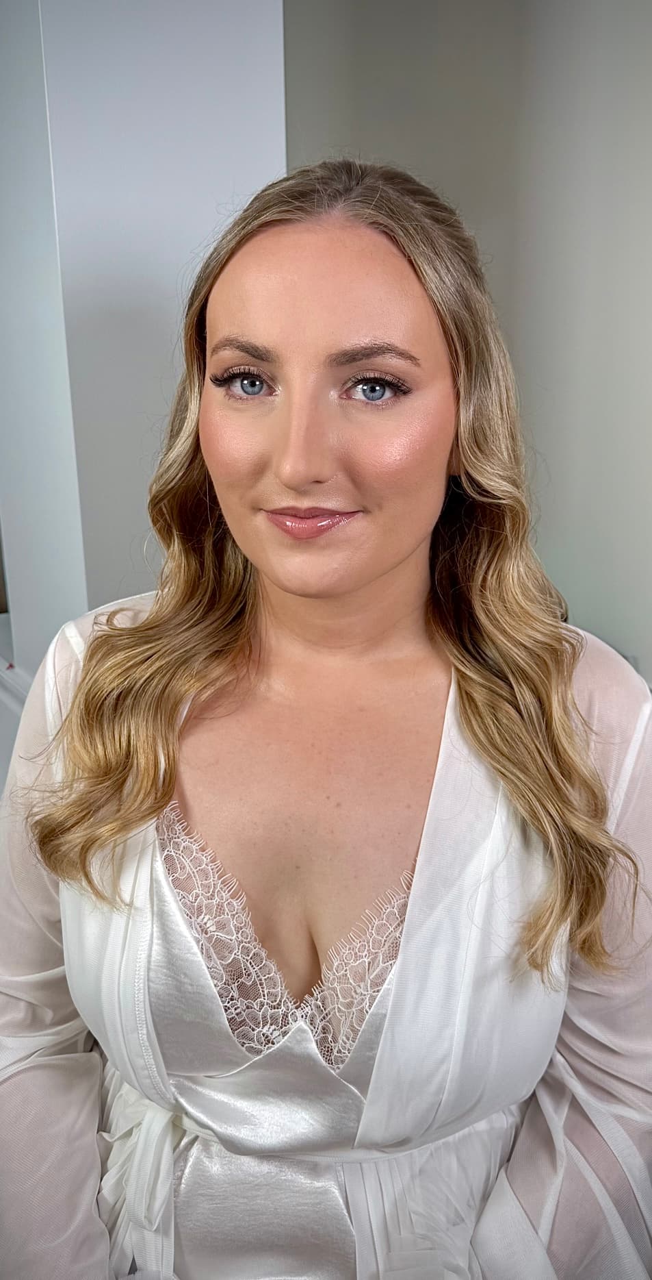 Bride with soft waves in honey blonde hair and natural glam makeup featuring defined eyes and nude lips.