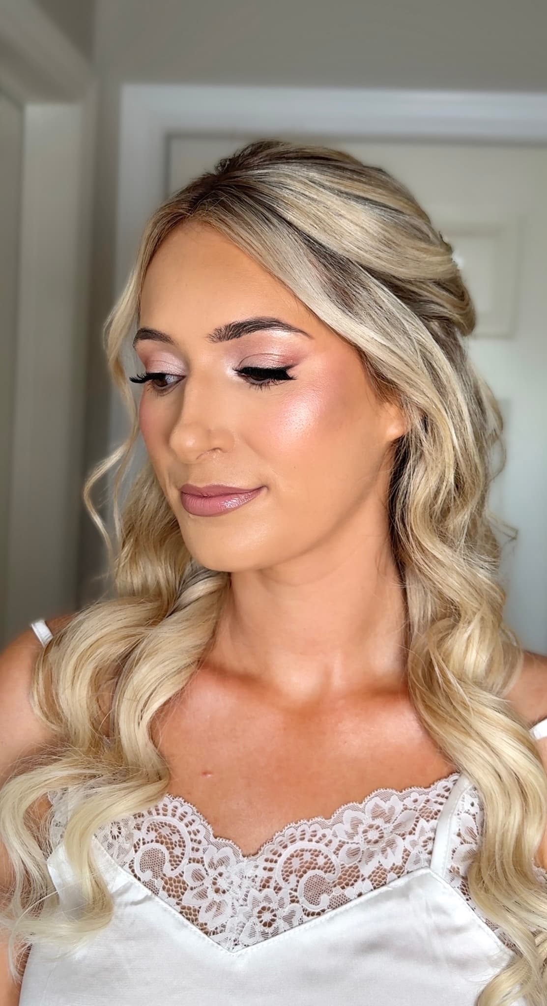 Bride with soft waves, side-swept blonde hair, peachy eyeshadow, winged liner, and mauve lip makeup.